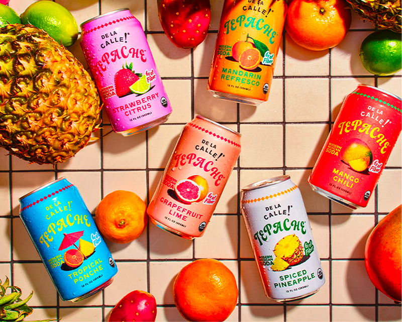 De La Calle TePache cans in various flavors surrounded by fruits on a tiled surface