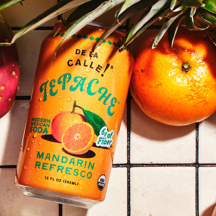 Tepache can with oranges and a pineapple on a tiled surface