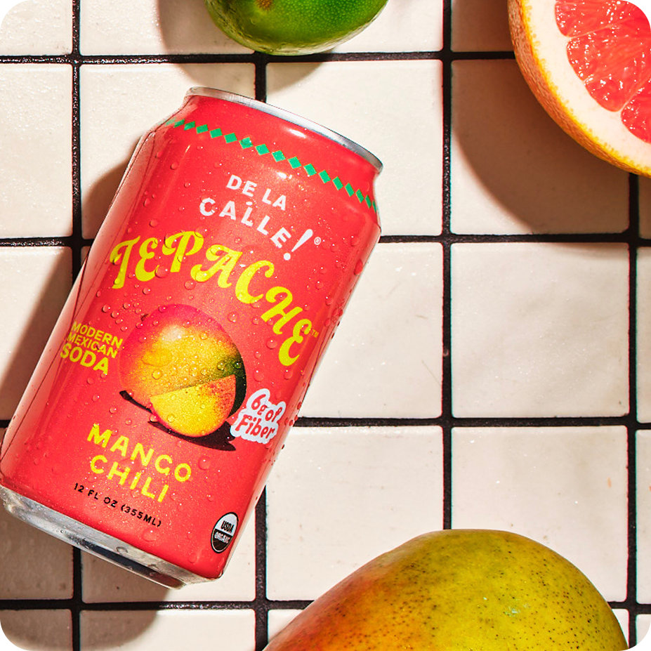 Red can of Tepache Mango Chili soda on a grid background with fruits.